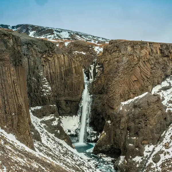 Litlanesfoss şelalesi Doğu İzlanda 'daki bazalt sütunlar ve karlı araziler tarafından çerçevelenmiştir.