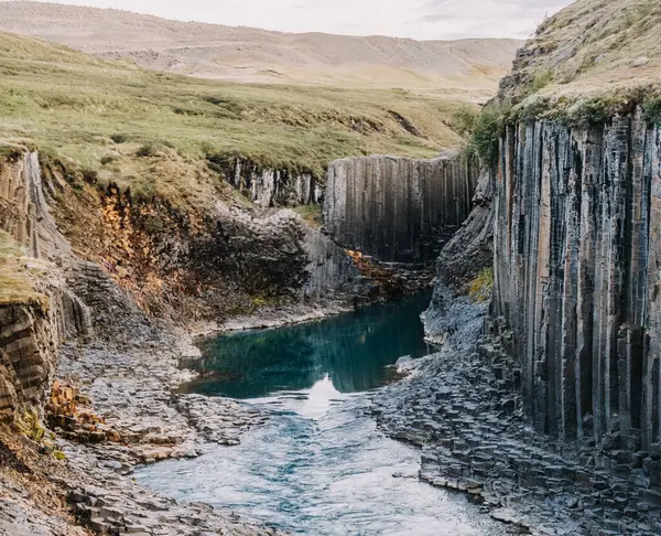 Studlagil Kanyonu 'ndaki bazalt uçurumlarından akan turkuaz buzul nehri.
