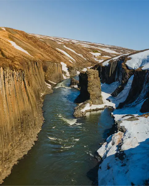 Doğu İzlanda 'daki Studlagil Kanyonu' nda kar yamaçları ve bazalt kayalıkları var.