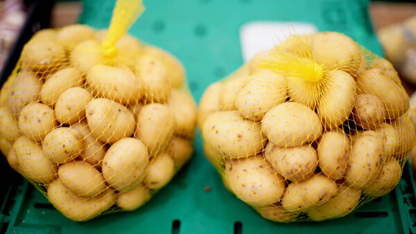 картофель лежит в пластиковых сетях на зеленой коробке на рынке