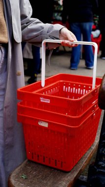 Bir kadının eli, çiftçi pazarından kırmızı bir market sepeti alır.