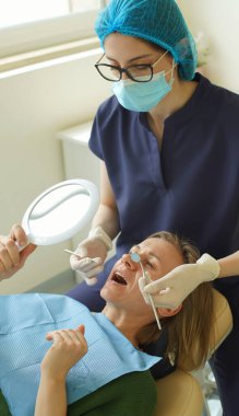 Doktor dişleri için implantların rengini seçerken hasta elinde tuttuğu aynaya bakar. Yumuşak odaklanma. Yakın plan