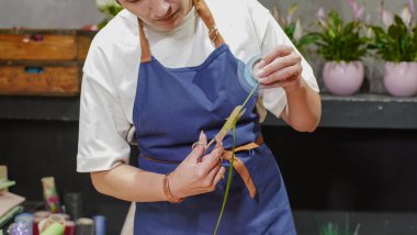 Çiçekçi çalışıyor. Dişi bir çiçekçi dekorasyon için kurdele ölçer. Küçük bir iş. Sahibi. Yakın plan