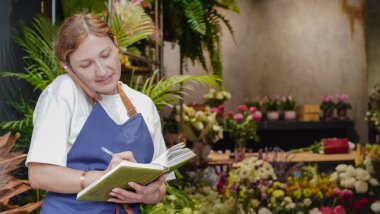 Çiçekçi not defterine iş notları yazar. Küçük bir iş. Yakın plan.