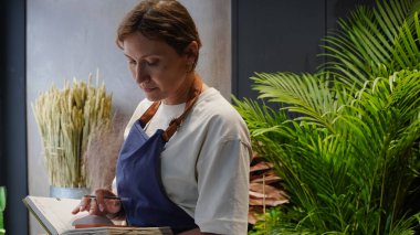 Çiçekçi not defterine iş notları yazar. Küçük bir iş. Yakın plan.