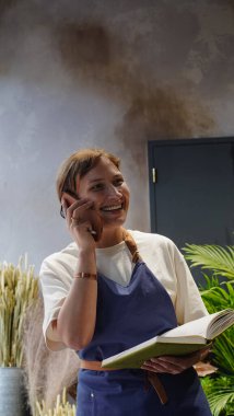 Çiçekçi telefonda konuşuyor, gülümsüyor ve not defterine iş notları yazıyor. Küçük bir iş. Yakın plan.