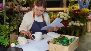 Bir çiçekçinin sahibi bir masada otururken belgeleri gözden geçiriyor ve kahve içiyor. Küçük bir iş. Yakın plan