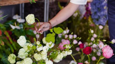 Çiçekçinin eli renkli bir buketten beyaz bir gül çıkarır. Küçük bir iş. Yakın plan