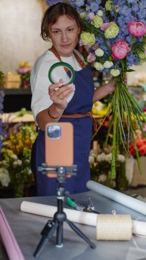 Çiçekçi, internetten buket yapmak için üç ayaklı bir masaya yerleştirilmiş bir telefonu kullanıyor. Çiçekçi eğitici bir video kaydediyor. Küçük bir iş. Yakın plan. Kullandığı kaseti gösteriyor.