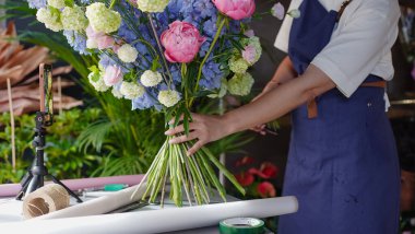 Çiçekçi, internetten buket yapmak için üç ayaklı bir masaya yerleştirilmiş bir telefonu kullanıyor. Çiçekçi eğitici bir video kaydediyor. Küçük bir iş. Yakın plan