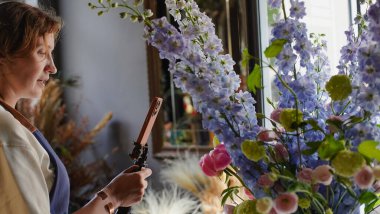 Çiçekçi internet üzerinden buketler yapmak için telefon kullanıyor. Çiçekçi kameraya bakarken eğitici videoları kaydeder. Küçük bir iş. Yakın plan.