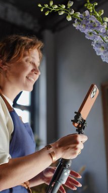 Çiçekçi internet üzerinden buketler yapmak için telefon kullanıyor. Çiçekçi kameraya bakarken eğitici videoları kaydeder. Küçük bir iş. Yakın plan.