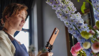 Çiçekçi internet üzerinden buketler yapmak için telefon kullanıyor. Çiçekçi kameraya bakarken eğitici videoları kaydeder. Küçük bir iş. Yakın plan.