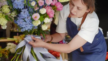 Çiçekçi bir buketi kurdeleyle süslüyor. Küçük bir iş. Yakın plan.