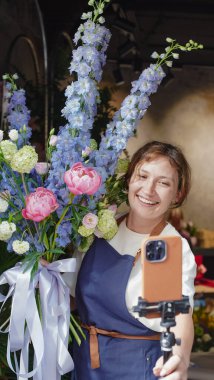 Çiçekçi internet üzerinden buketler yapmak için telefon kullanıyor. Çiçekçi kameraya bakarken eğitici videoları kaydeder. Küçük bir iş. Yakın plan.