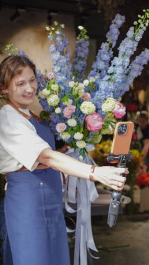 Çiçekçi internet üzerinden buketler yapmak için telefon kullanıyor. Çiçekçi kameraya bakarken eğitici videoları kaydeder. Küçük bir iş. Yakın plan.