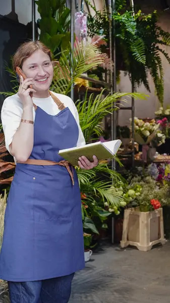 Çiçekçi telefonda konuşuyor, gülümsüyor ve not defterine iş notları yazıyor. Küçük bir iş. Yakın plan.