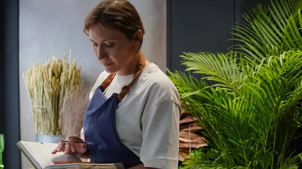 Çiçekçi not defterine iş notları yazar. Küçük bir iş. Yakın plan.