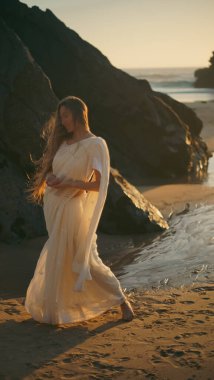 Beyaz elbiseli güzel bir kadın sahilde dans ediyor.