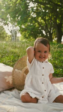 Küçük kız parkta battaniyenin üzerinde otururken büyük bir hasır şapkayla oynuyor. Yumuşak odaklanma. Yakın plan