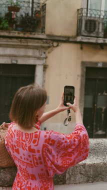 Parlak elbiseli bir kadın cep telefonuyla Lizbon sokaklarının fotoğrafını çekiyor. Yumuşak odak.