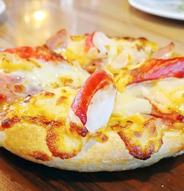 Pastırmalı, ananaslı ve yengeçli taze Hawaii pizzasının yakın plan görüntüsü. Pizza ahşap bir masanın üzerinde ve kabuğu kahverengi ve çıtır çıtır..