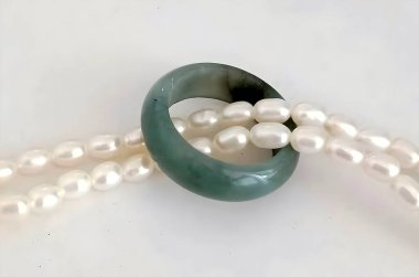 Zarif bir yeşim yüzüğün yakın plan görüntüsü parıltılı inci iplikçikleriyle sarmalanmış, ince mücevher tasarımının güzelliğini ve inceliğini gözler önüne seriyor..