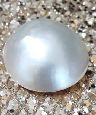 A stunning white mabe pearl resting on a sparkling surface, showcasing its lustrous texture and natural beauty. Perfect for jewelry and fashion imagery. clipart