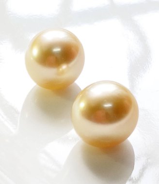 Bu resimde, doğal güzelliklerini ve zarafetlerini vurgulayan yansıtıcı bir yüzeyde iki altın deniz incisi sergileniyor. Moda ve lüks temalar için mükemmel.