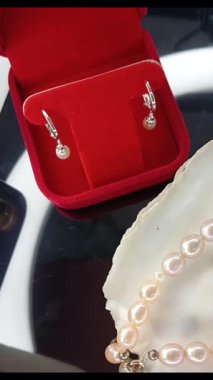 Bu resimde zarif bir inci mücevher seti, parlak bir yüzeyde kırmızı kadife bir kutuda güzelce sergilenen küpeler ve bir kolye sergilenmektedir. Hediye için mükemmel..