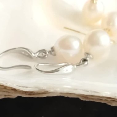 Yumuşak bir yüzeyde zarif inci küpeler ve narin renkler.