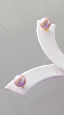 Zarif pembe inci küpeler şık bir mücevher standında sergileniyor.