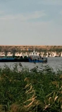 Moldova 'da bir nehri geçen feribot, önü sazlıklarla çevrili doğal manzaralar ve açık bir gökyüzünün altındaki uçurumlarla çevrili. Yüksek kalite 4k görüntü