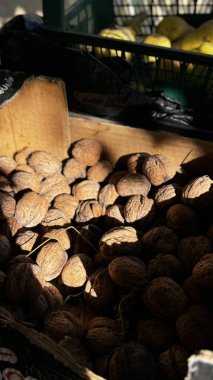 Kurumuş cevizlerle dolu ahşap bir sandık yerel bir pazarda, parlak güneş ışığıyla aydınlatılmış, yakındaki gölgelerde filtrelenmiş, zengin bir hasat zamanı sergiliyor..
