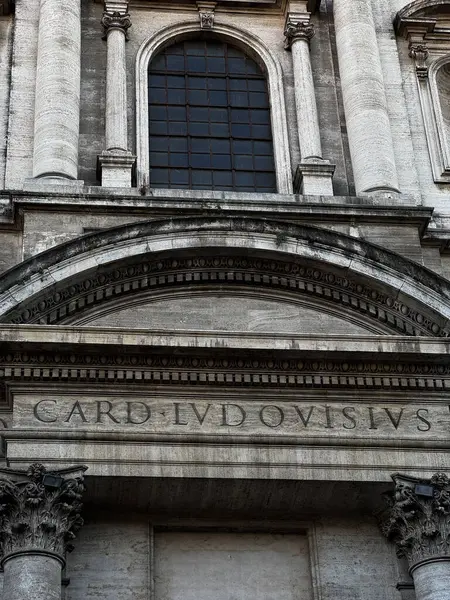Oyma taş yazıtlar tarihi bir binanın girişini dekore ediyor, hareketli bir şehirde uzun kemerler ve geniş pencerelerle karışık mimari tarzlar sergiliyor..