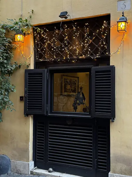 Tarihi bir binanın büyüleyici penceresi açık, üzerinde peri ışıkları asılı sıcak bir iç mekan sergileniyor. Yumuşak aydınlatma gecenin davetkar atmosferini arttırır..