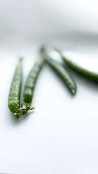 Beyaz bir zemin üzerinde taze bezelye kabuklarının yakın çekimleri, sığ alan derinliği, sağlıklı beslenme kavramları için ideal. Yüksek kalite fotoğraf
