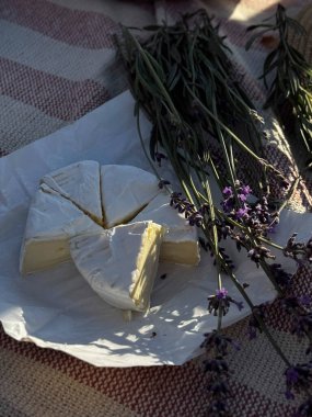 Damalı piknik battaniyesinde dilimlenmiş peynir ve lavanta..