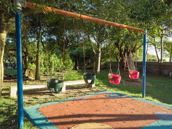 Sessiz bir parkta ağaçlar ve sıcak bir akşam güneşi altında dört çocuk sallanıyor.