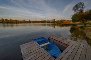 Mavi bir tekneyle iskele manzarası, sisli sonbahar gökyüzü, sarı yapraklar.