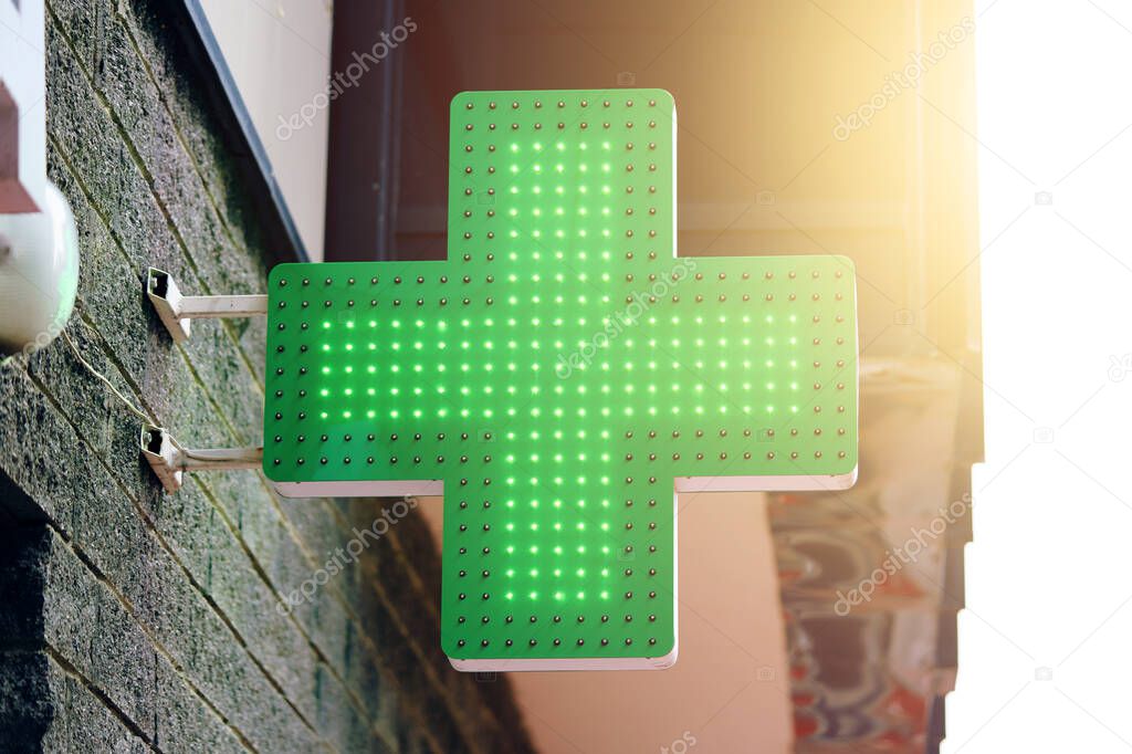 Drugstore signboard on building. Pharmacy green light cross board. Store decoration of downtown. Logo of city dispensary. Sunlight on background.