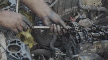 Tamirci çıplak elleriyle motorun camdaki zincir makarasını cırcırla sıkıyor.