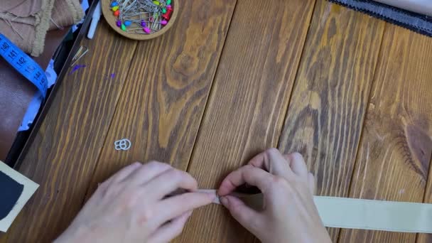 女人的手指把生态皮革的带子折成两半 然后用夹子把它固定起来 木制桌子上缝纫工艺的头像 业余爱好和手工艺 — 图库视频影像