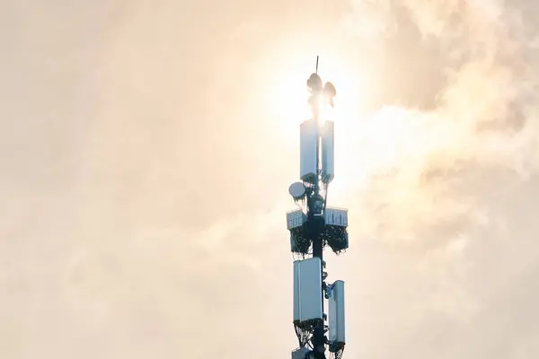 LTE radio network communication equipment with wireless modules and smart antennas mounted on metal pillar on clouds and sun sky background. Telecommunication tower of 4G and 5G cellular.