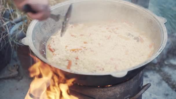 用米饭 肉和蔬菜做的东方菜品 厨师用开槽勺子把皮面包和大锅混合在一起 在篝火边做饭 穷人的慈善午餐 卡赞的Plov闻起来好香 — 图库视频影像