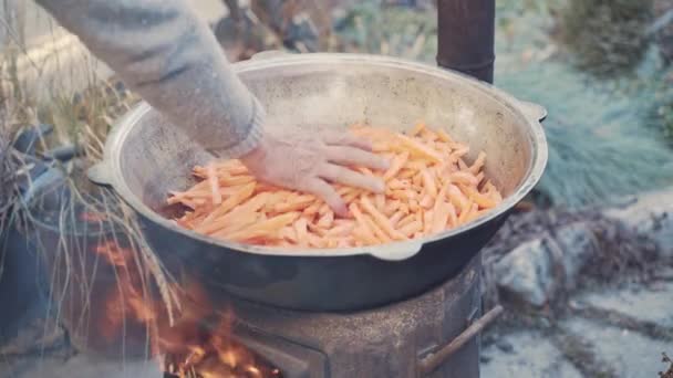 人类把一把切好的胡萝卜倒进大锅里 用肉和沸腾的油搅拌 然后用手均匀地分发蔬菜 用篝火煎东方菜 旅游营的厨房 — 图库视频影像