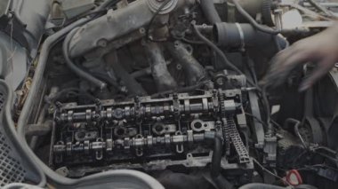 Bir atölyede bir araba motorunu tamir eden mekanik elin yakın çekimi, ayrıntılı bileşenleri görünür..