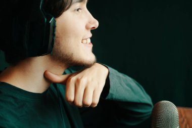 Genç bir adam, gülümsüyor, mikrofon ve kulaklıkla düşünceli poz veriyor, yaratıcılığını gururla sergiliyor.