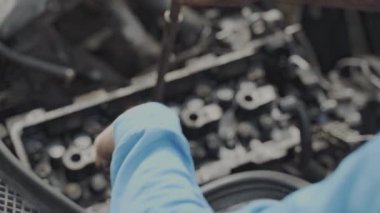 Atölyedeki bir araba motoru üzerinde çalışan bir tamircinin yakın çekimi, ayrıntılı otomotiv tamirini gösteriyor.
