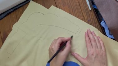 Kadın eli, etnik bir saç aksesuarı yaratır. Needlewoman siyah kalemle kumaşın üzerindeki tacın plastik şeklini özetliyor. Ahşap bir masanın üzerinde eko deri ve dikiş aletleri. Hobiler ve el sanatları.